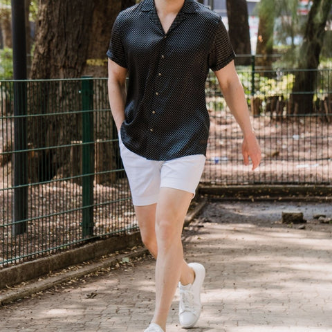 photo of a model wearing white shoes white shorts and a black dotted short sleeve silk shirt from 1000 kingdoms