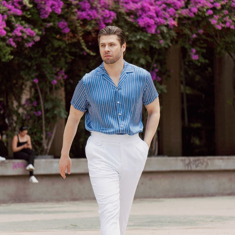 model walking through a plaza wearing white high rise pants and a tucked in short sleeve blue stripe silk shirt from 1000 kingdoms