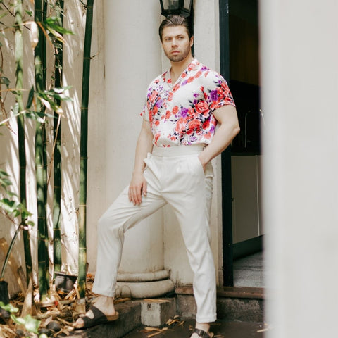 model standing in the garden wearing brown leather sandals white pants and a short sleeve white floral silk shirt from 1000 kingdoms