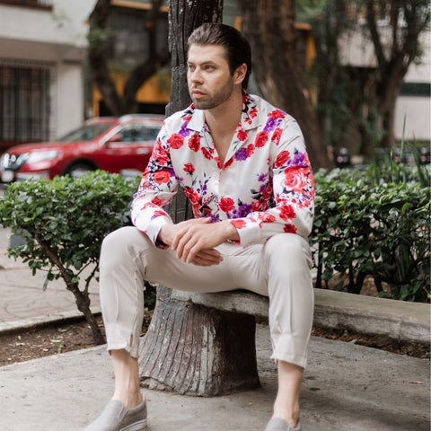 model sitting on a bench in the park wearing grey slip on shoes khaki pants and a long sleeve white floral silk shirt from 1000 kingdoms