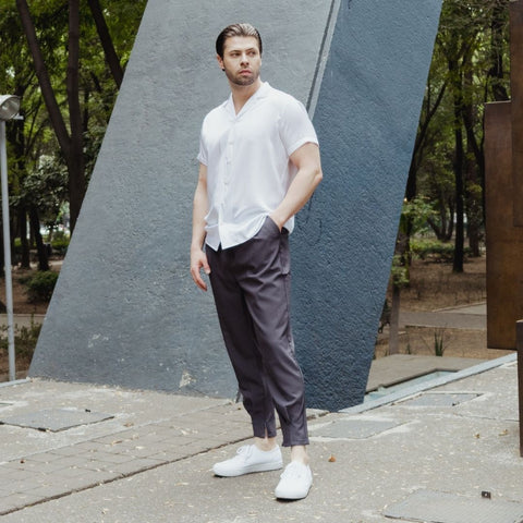 model standing in a plaza wearing white shoes grey pants and a short sleeve white silk shirt from 1000 kingdoms